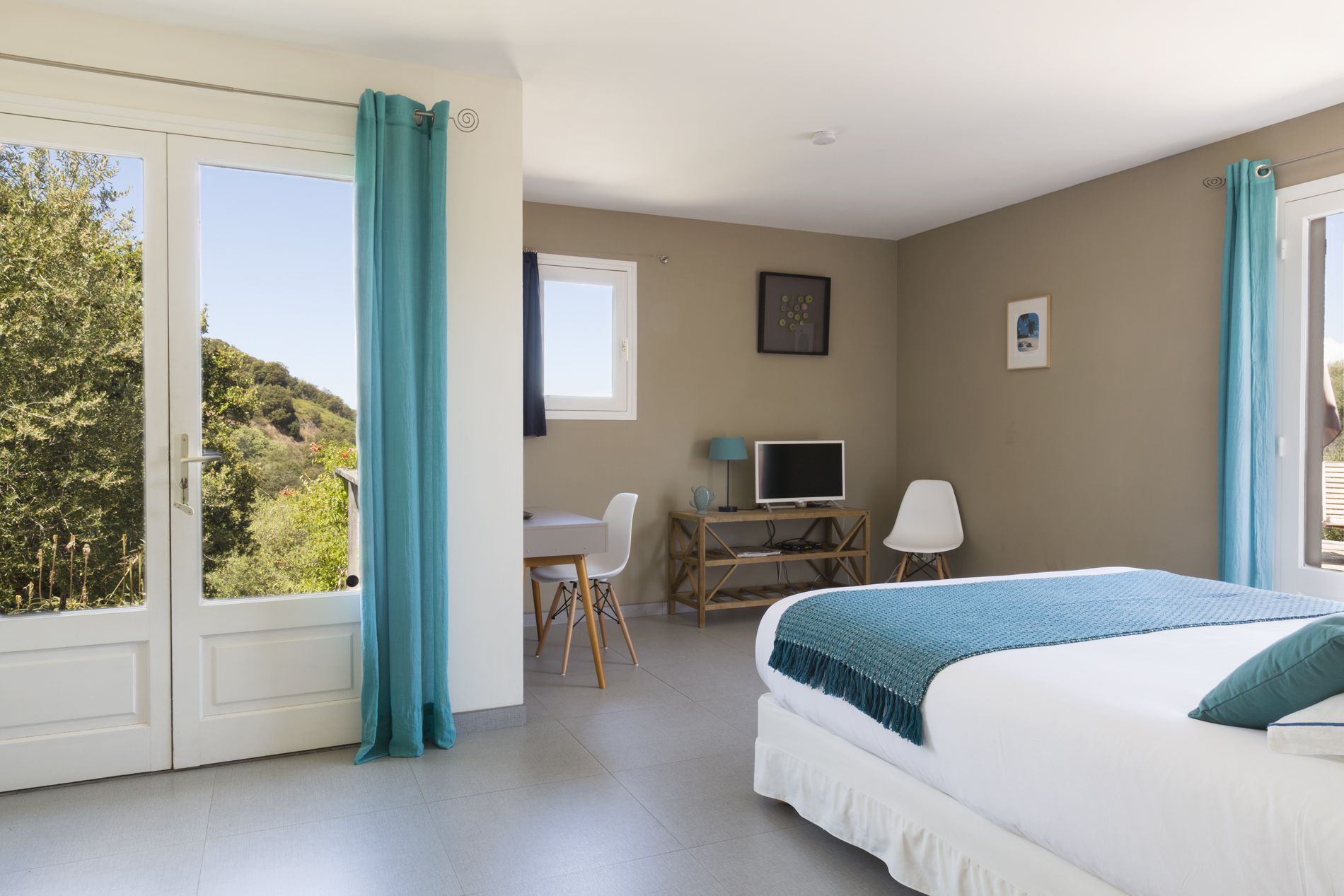 Un dormitorio con una cama, un escritorio con una computadora y vistas a la vegetación exterior.