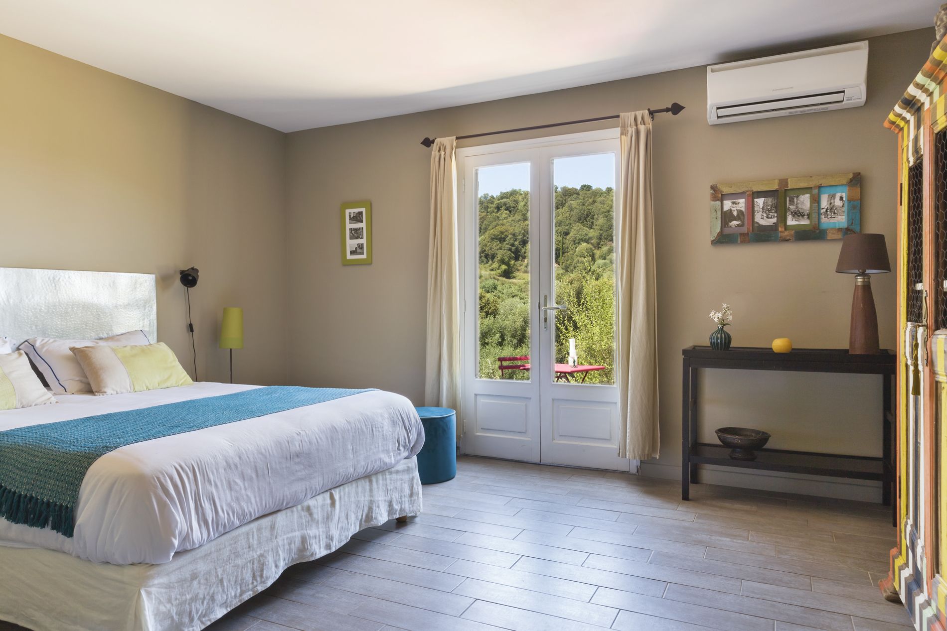 A bedroom with a bed, a bedside table, an air conditioner, and a window with curtains.