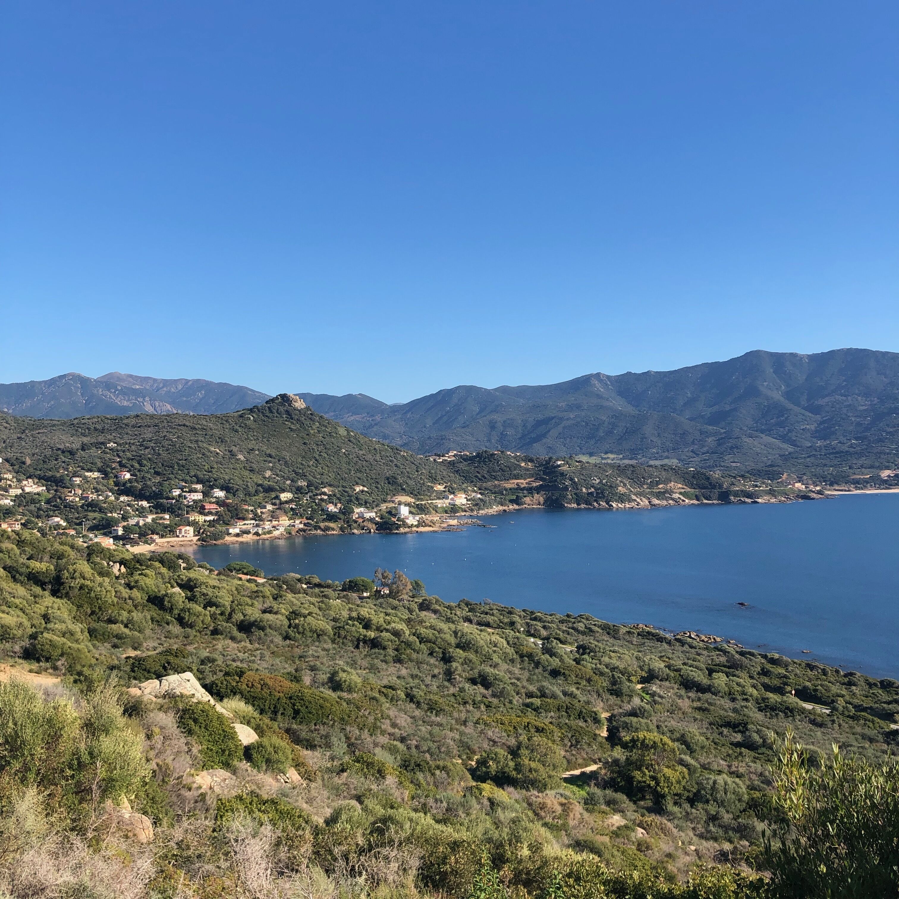 Un paysage côtier offrant une vue dégagée sur la mer, les collines et quelques bâtiments dispersés.