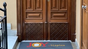 A wooden double door with a plaque reading "JOY Naples" and a doormat with the same name. - Joy Naples (Naples)
