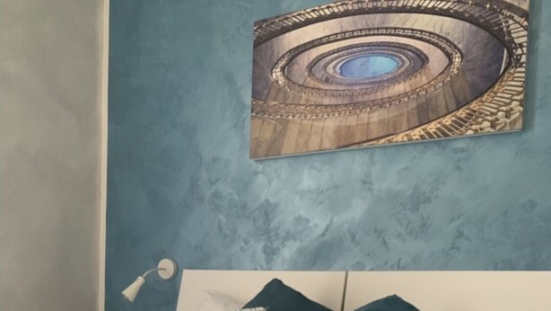 A hotel room with a bed, a tray with croissants, a cup of coffee, and a painting on the wall. - Joy Naples (Naples)