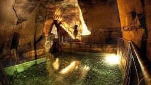 A dimly lit cave with a water-filled pool, stone walls, and a staircase leading to a higher level. - Joy Naples (Naples)