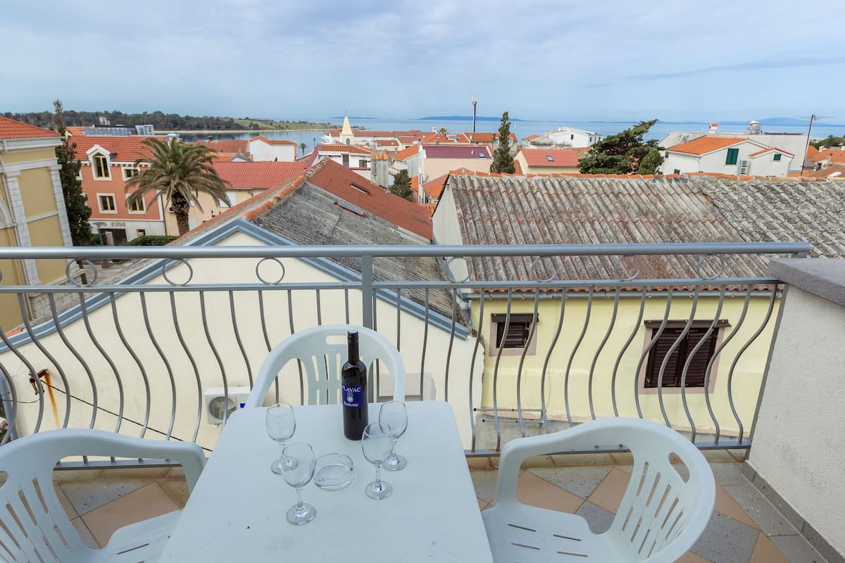 A balcony with a table set for two, a bottle of wine, and a view of the town.