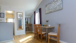 A dining area with wooden chairs and a table, a clock on the wall, and a window with curtains. - Apartments in City Center Ventus (Novalja)