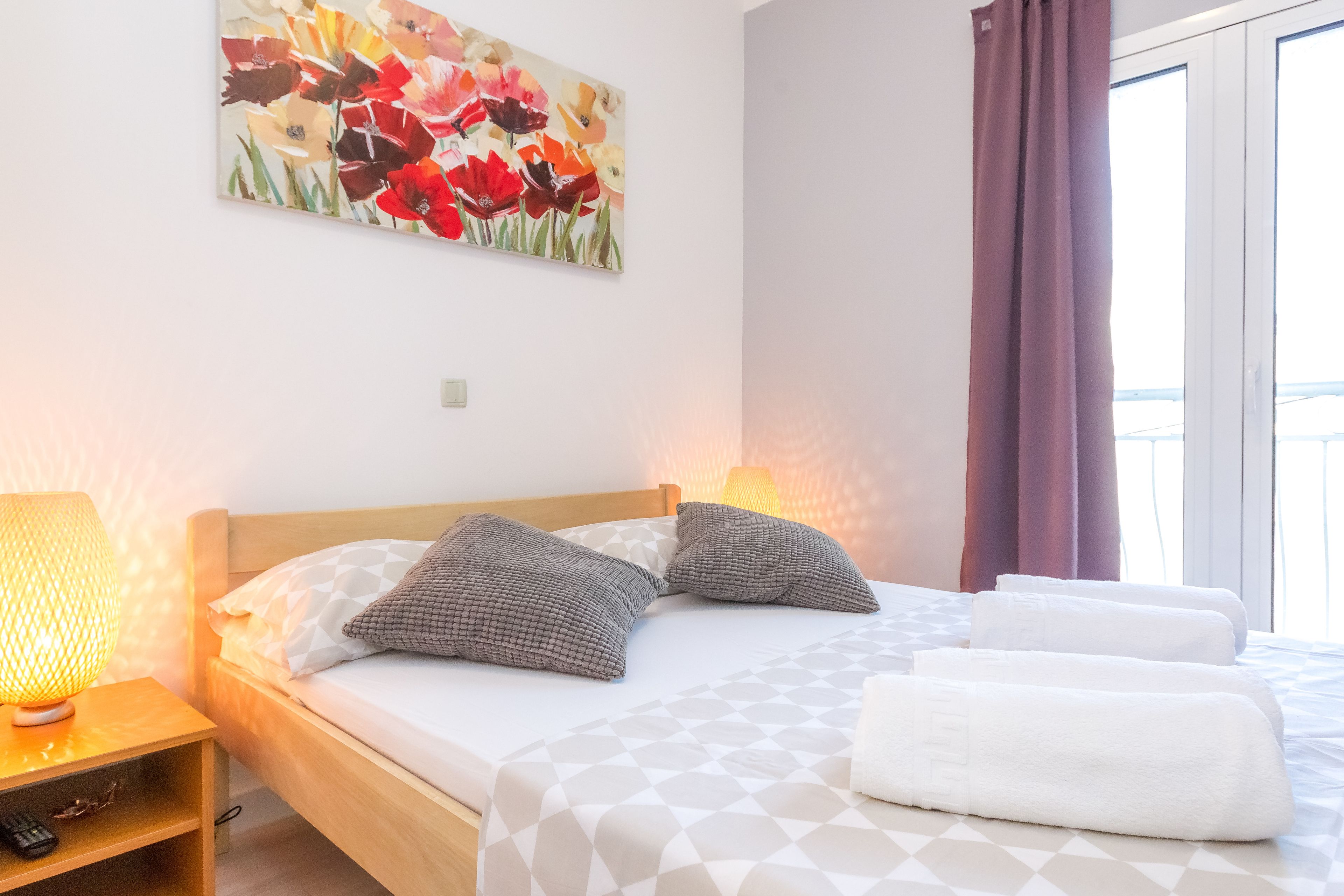 A neatly made bed with a geometric patterned bedspread, two pillows, and a bedside lamp on a wooden nightstand.