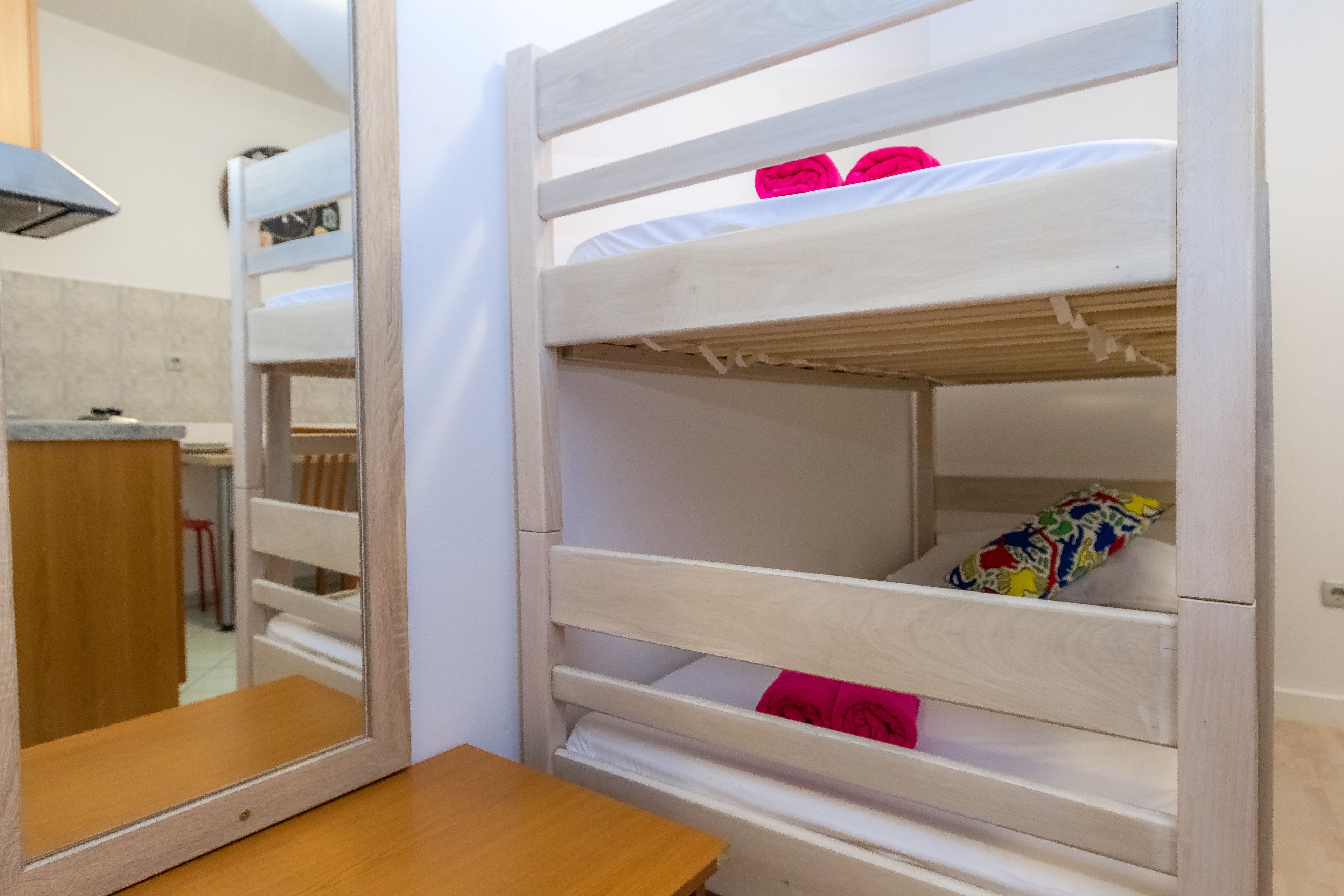 A bunk bed with two levels, a wooden table, and a mirror.