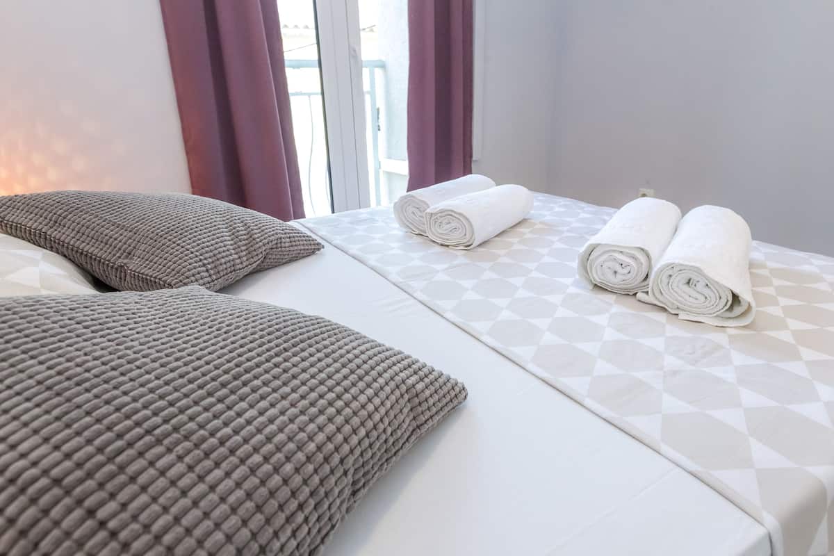 A hotel room with a bed, two pillows, and two rolled towels.
