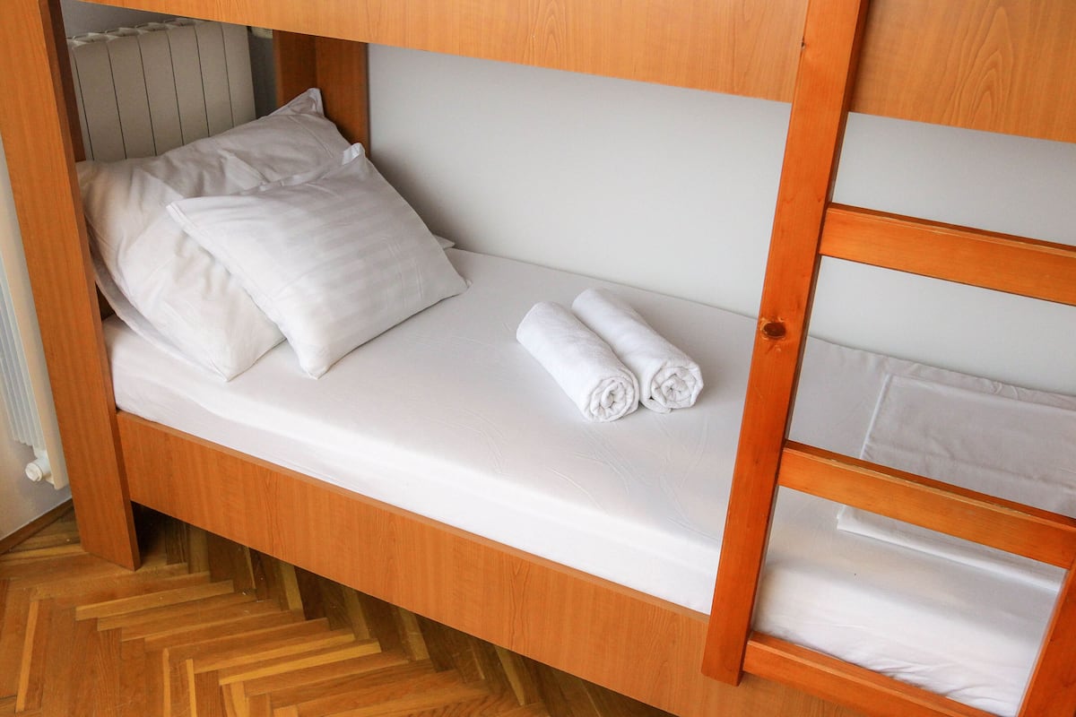 A wooden bunk bed with a mattress, pillows, and rolled towels.