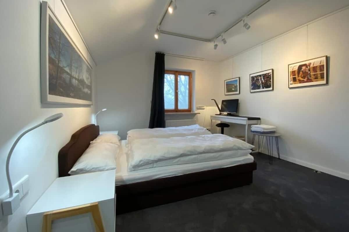 Et moderne soveværelse med seng, natbord, skrivebord, stol og kunst på væggene.