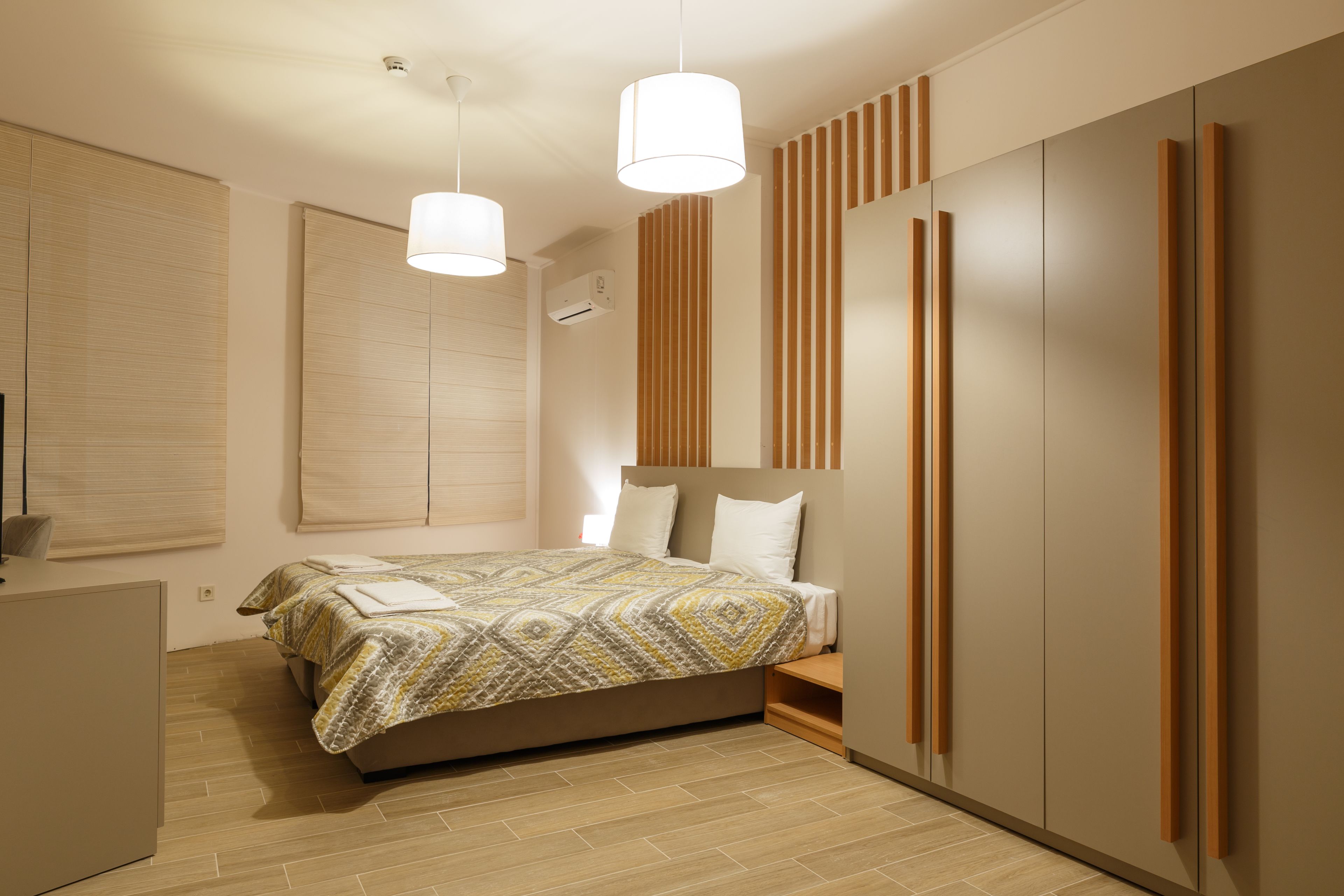 A modern bedroom with a bed, bedside tables, a wardrobe, and a window with blinds.