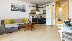 A modern kitchen with white cabinets, a microwave, and a stove. There's a dining area with a table and chairs, and a sofa with cushions. - Maru Apartments (Novalja)