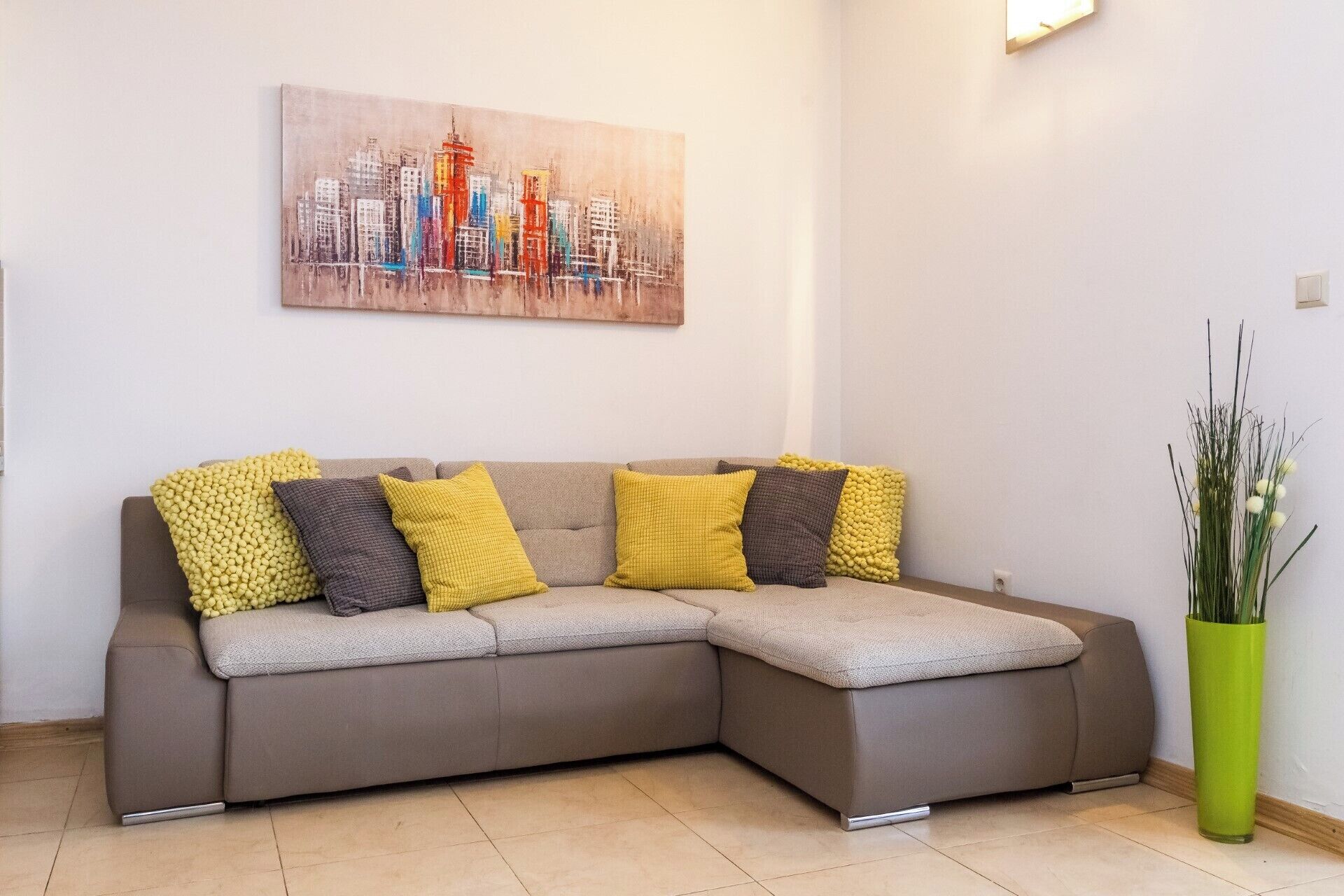 Ein modernes Wohnzimmer mit einem Ecksofa, einem Stadtbild-Gemälde und einer hohen, grünen Vase.