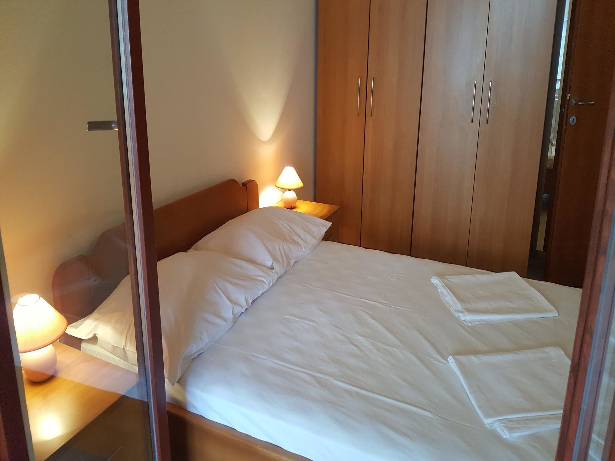 A neatly made bed with white linens, a wooden headboard, and a nightstand with a lamp.