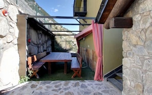 A stone-walled outdoor seating area with a table and benches, a wooden pergola, and a view of the surrounding landscape. - Casa Rural Borda Patxeta (Canillo)