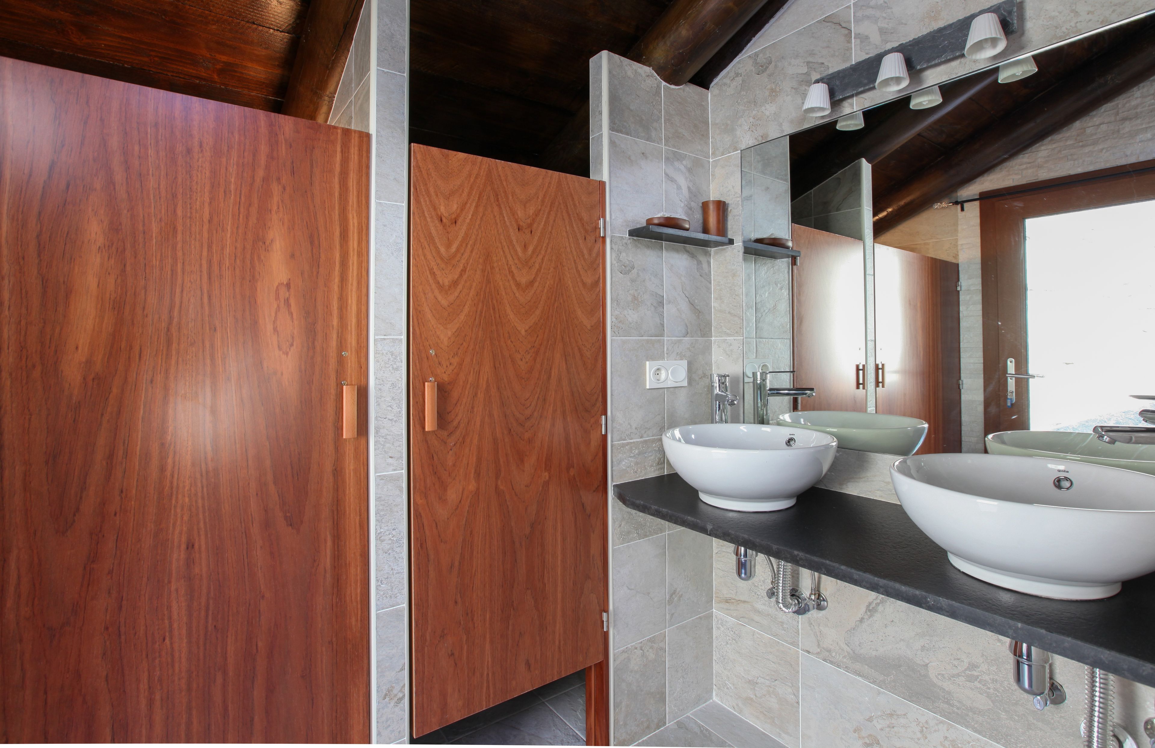 Un baño moderno con dos lavamanos grandes blancos, armarios de madera y un espejo amplio.
