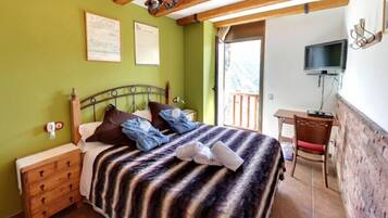 Un dormitorio con cama, mesitas de noche de madera, un escritorio, televisor y puerta al balcón.