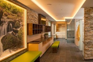A modern interior with a stone wall, a waterfall painting, and a bench. - Guthof Lutz Appartement mit kostenlosen Sommerbergbahnticket Mai bis Oktober (Schattwald)