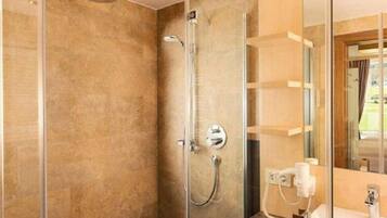 A modern bathroom with a glass shower enclosure, a visible towel dispenser, and a mirror reflecting the room.