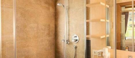 A modern bathroom with a glass shower enclosure, a visible towel dispenser, and a mirror reflecting the room.
