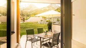 An outdoor patio with a table and chairs, a large umbrella, and a view of a mountain landscape. - Guthof Lutz Appartement mit kostenlosen Sommerbergbahnticket Mai bis Oktober (Schattwald)