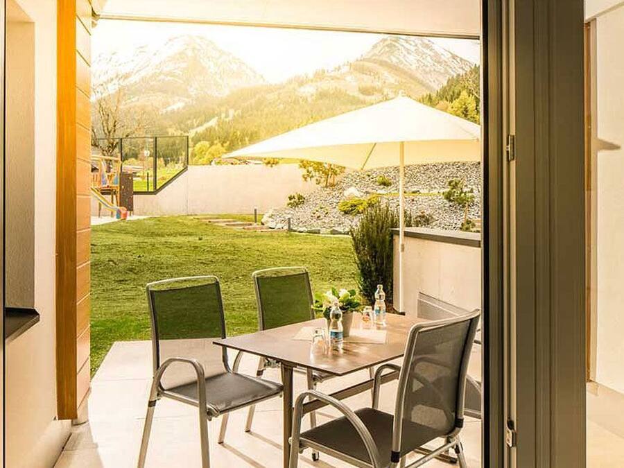 An outdoor patio with a table and chairs, a large umbrella, and a view of a mountain landscape.