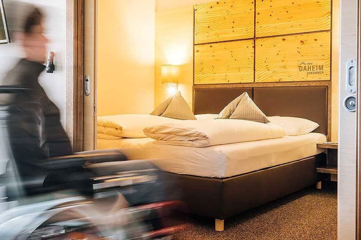 Una habitación de hotel con cabecera de madera, dos camas y una mesita de noche con lámpara.