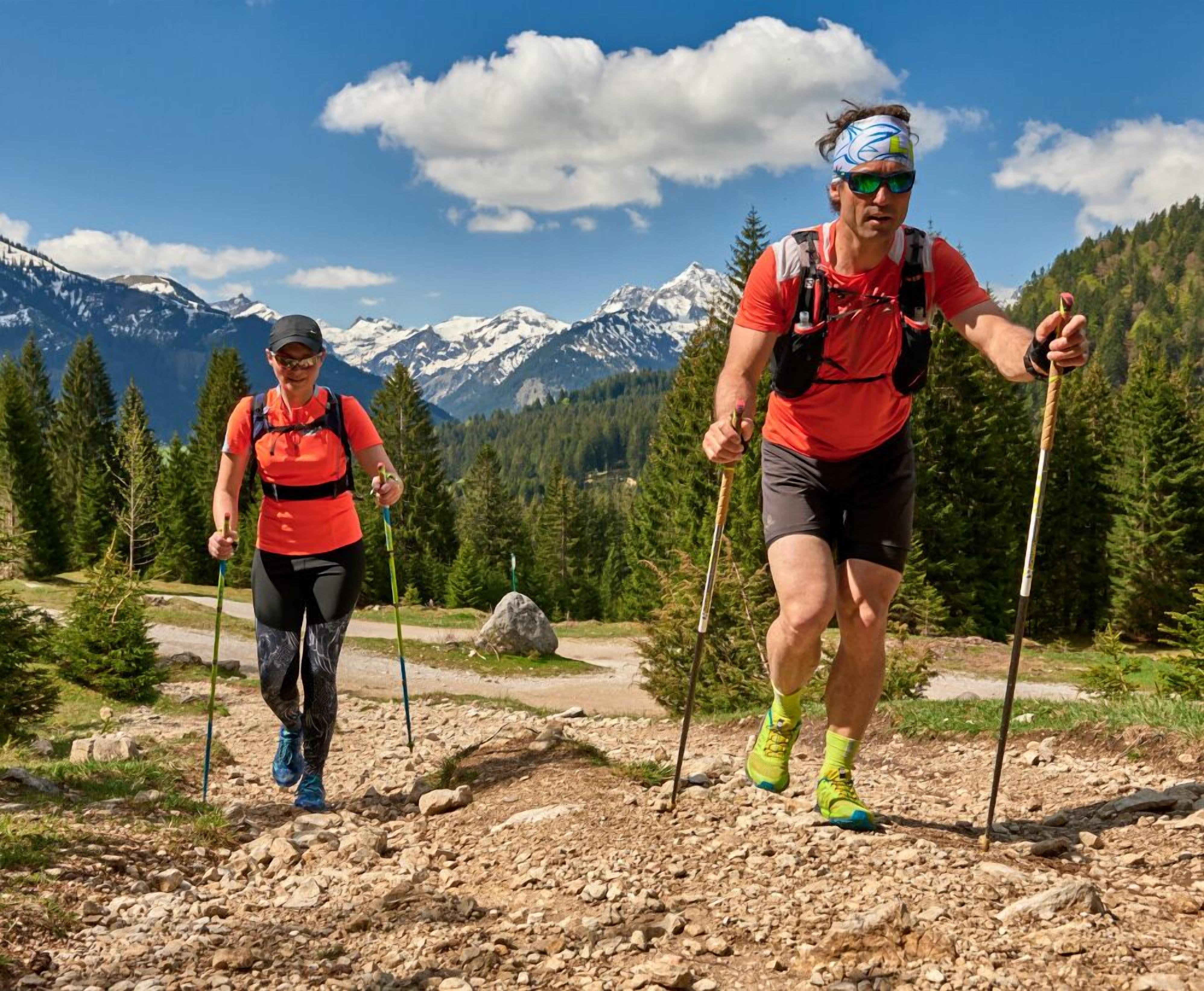 Deux personnes font de la randonnée sur un sentier rocailleux, avec une chaîne de montagnes en arrière-plan.
