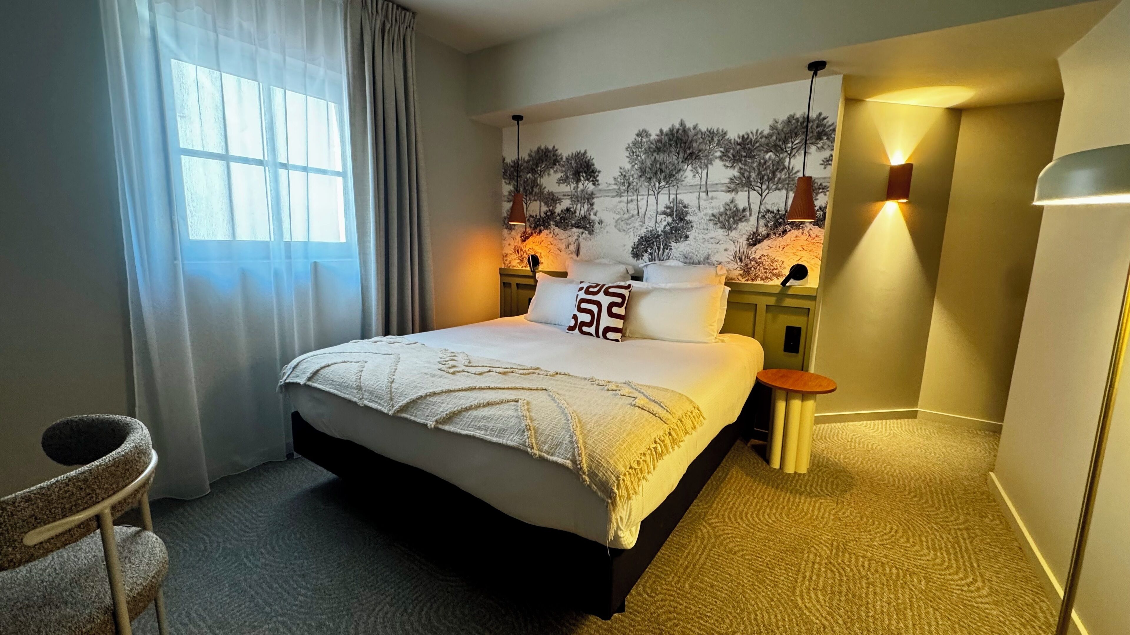 Een hotelkamer met een bed, een stoel, een wandlamp en een schilderij.