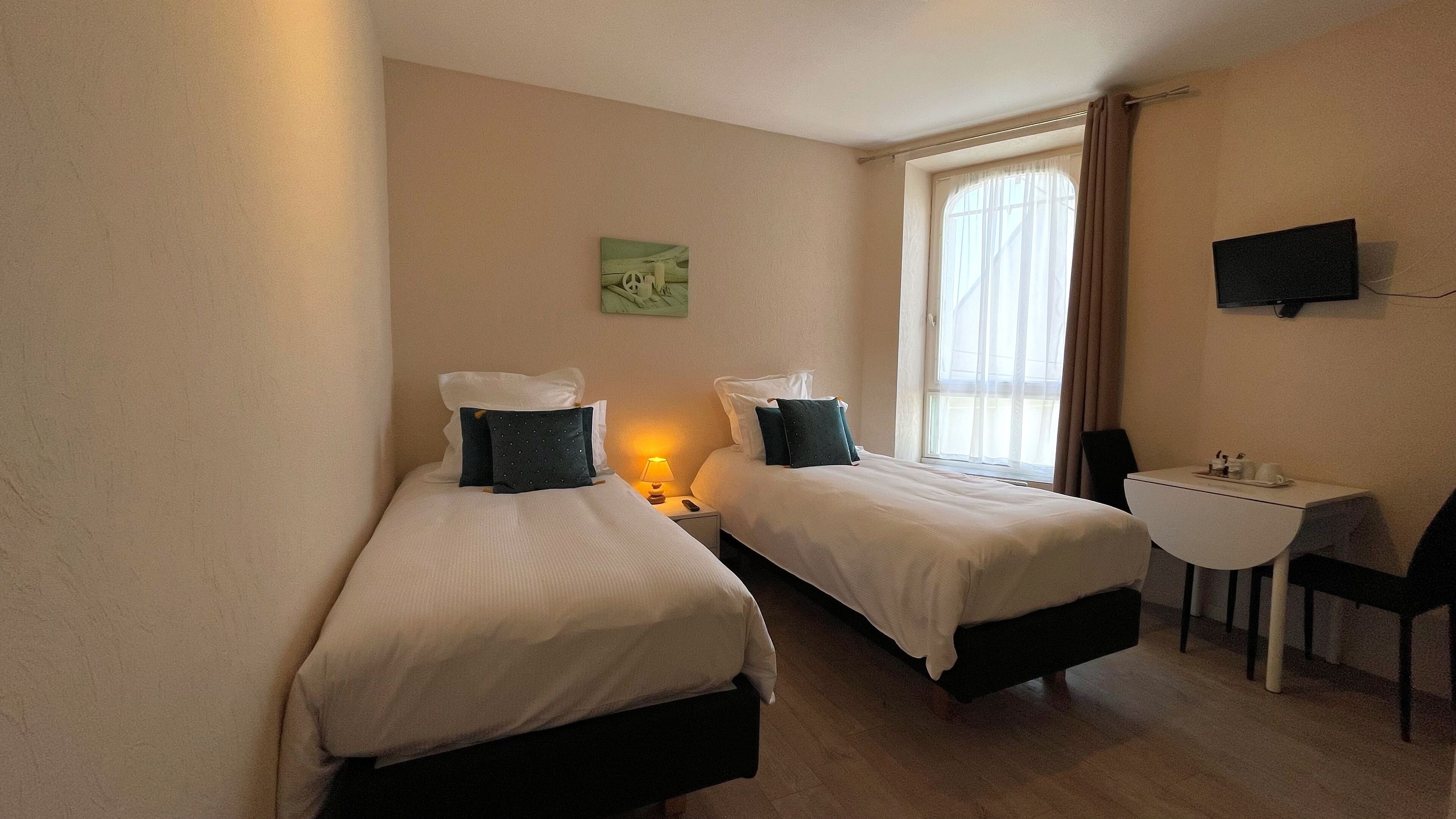 A hotel room with two single beds, a desk with a chair, a television on the wall, and a window with curtains.