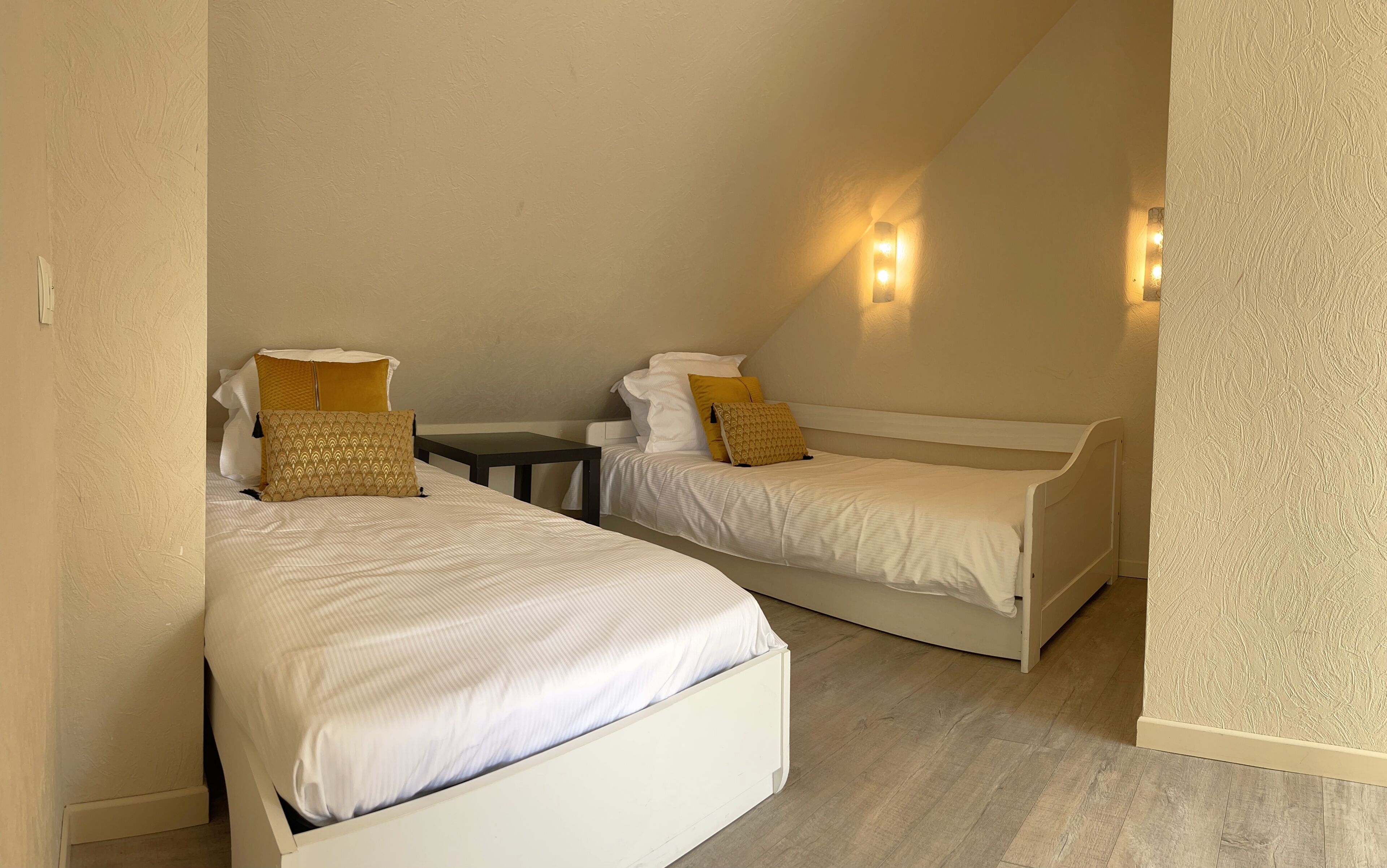 A room with two single beds, a small table, and wall-mounted lights.