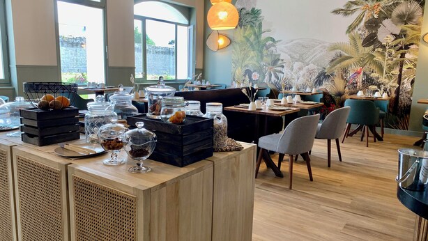 L’intérieur d’un restaurant, avec des tables et des chaises en bois, ainsi qu’un espace buffet où sont présentés différents plats.