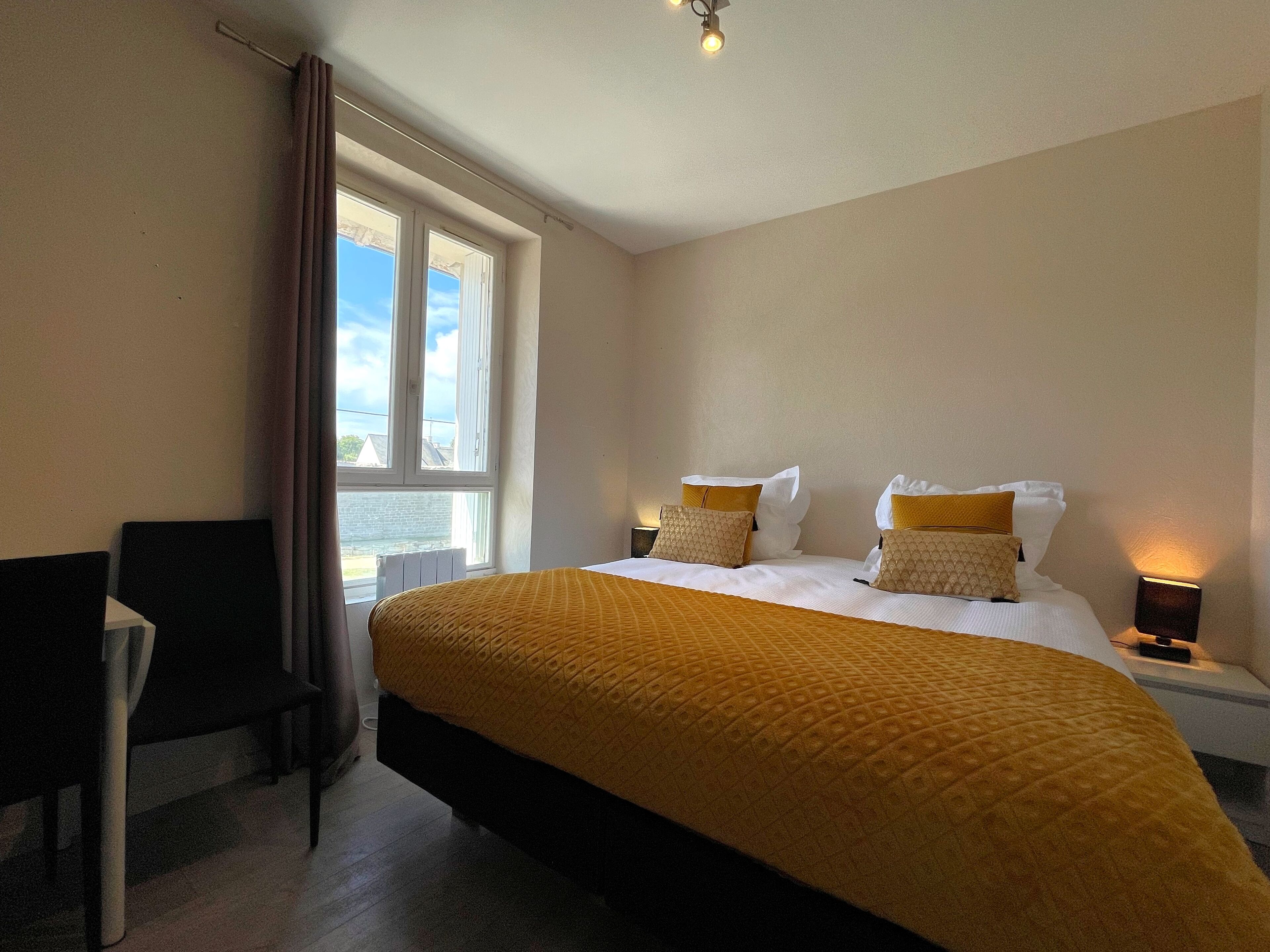A hotel room with a large bed, two bedside tables, a chair, and a window with curtains.