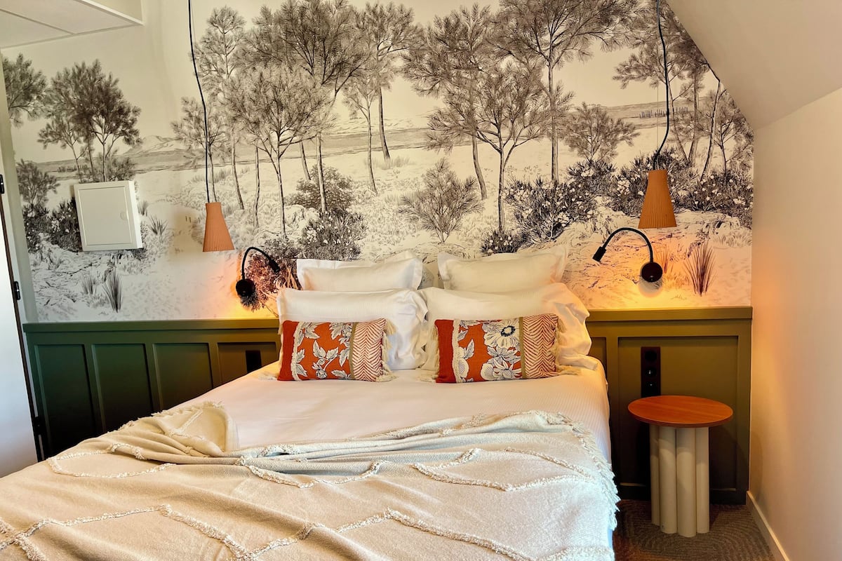 Une chambre à coucher avec un lit, des oreillers, une table de chevet, une lampe et une fresque murale.