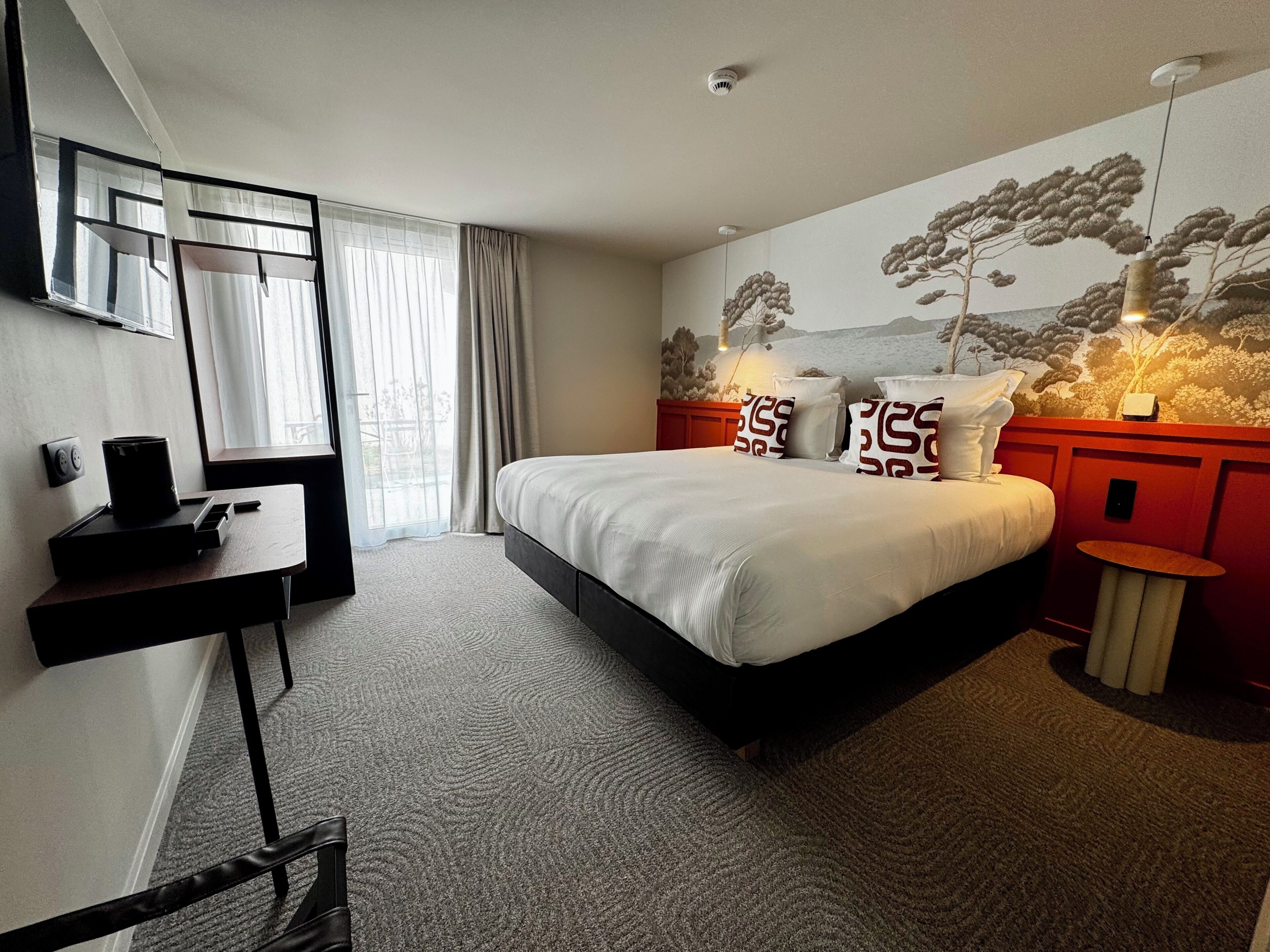 A hotel room with a bed, a desk, a mirror, and a wall mural.