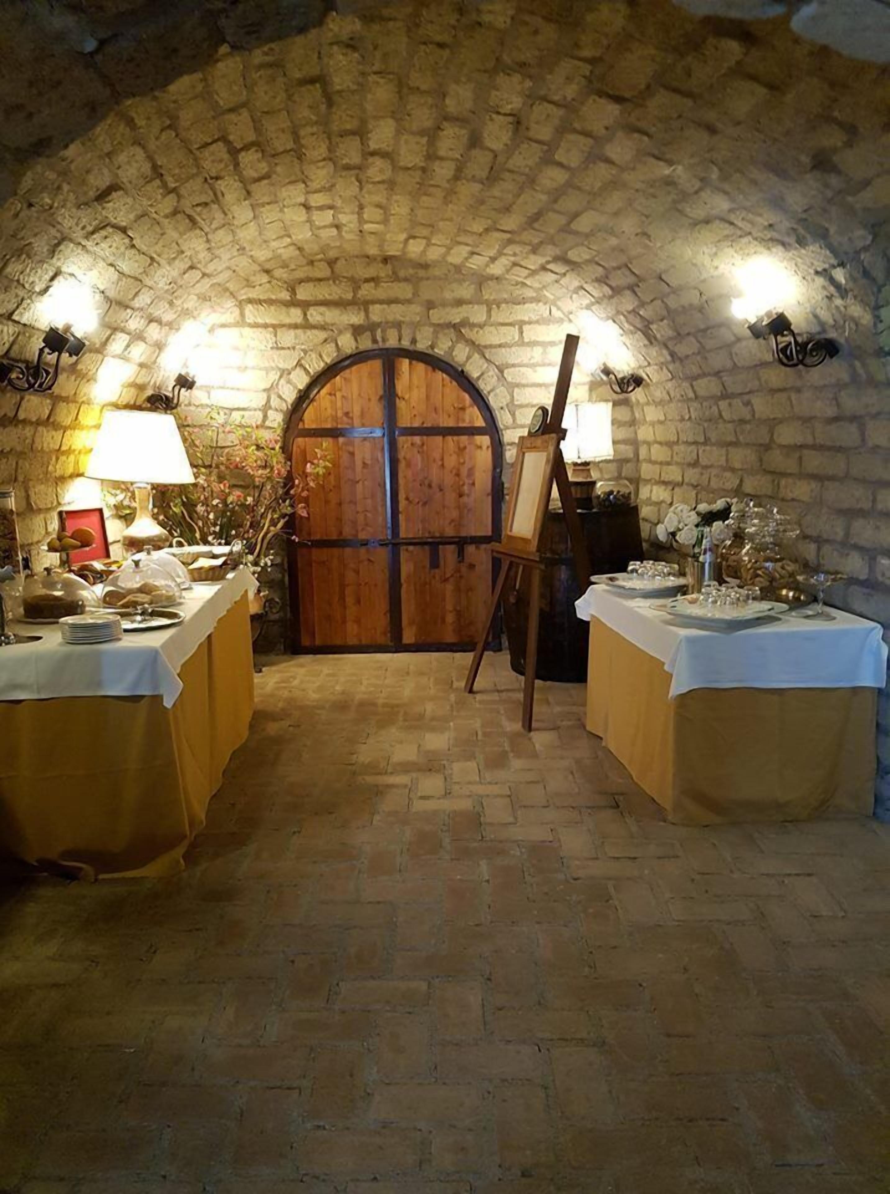 A rustic room with a vaulted stone ceiling, a wooden door, and tables set for a meal.