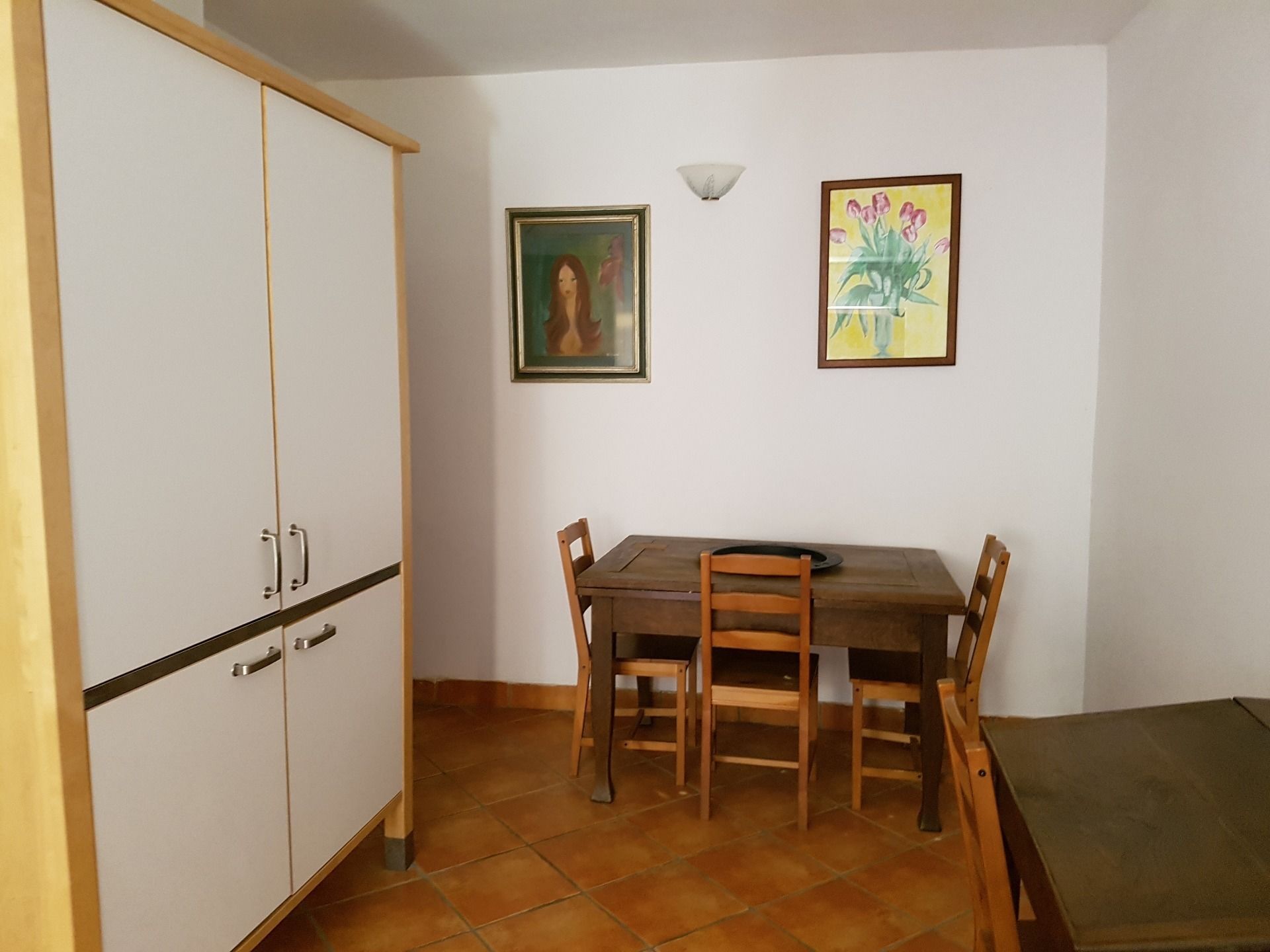 Zona pranzo con tavolo e sedie in legno, un armadietto bianco e due quadri appesi al muro.