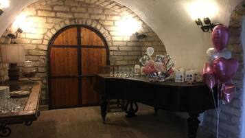 Una habitación rústica con paredes de piedra, una puerta de madera, una mesa con cristalería y globos, y una mesita con platos y vasos.