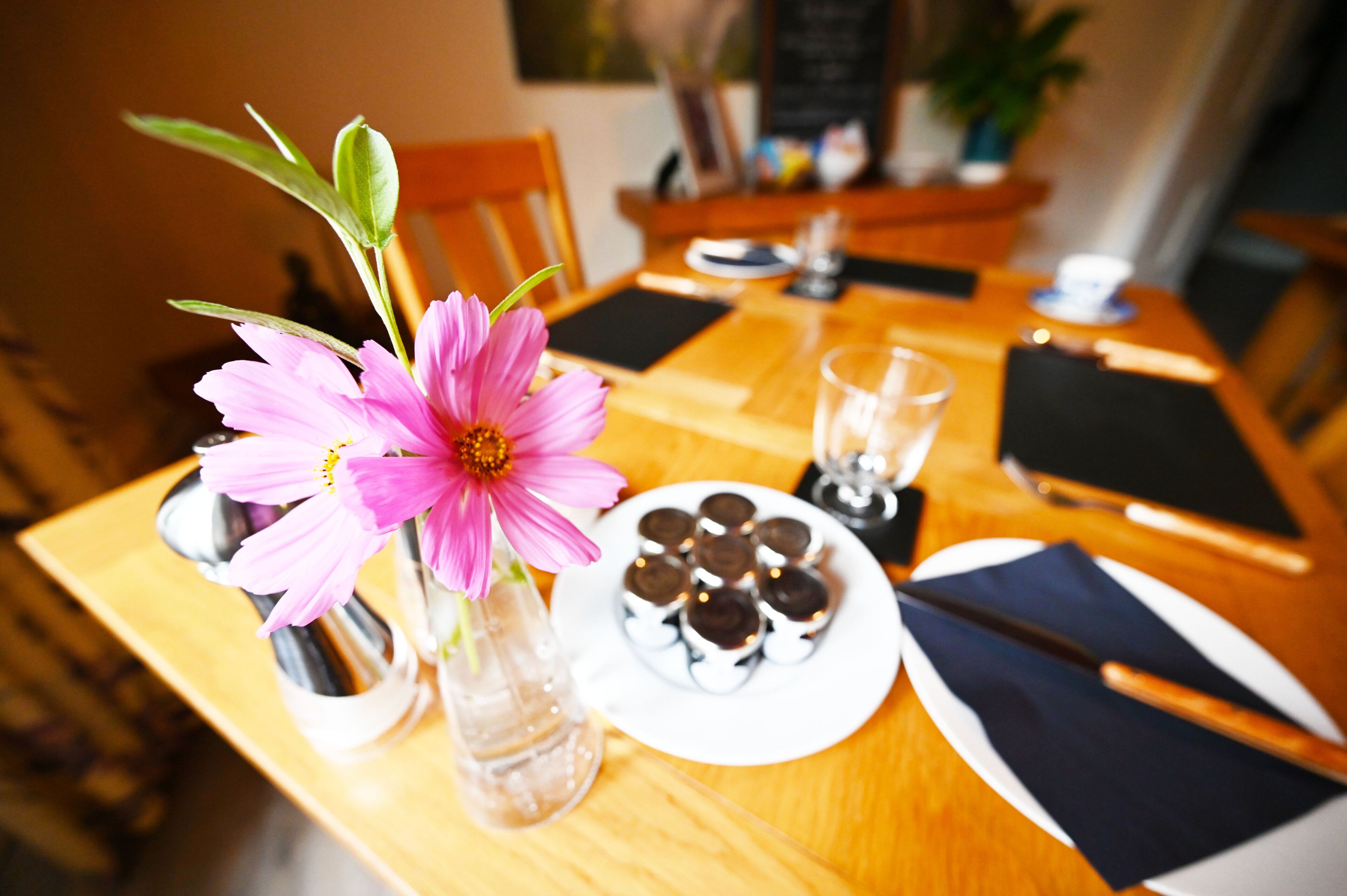 A dining table with a pink flower vase, a plate of chocolate-covered cookies, and a glass of water.