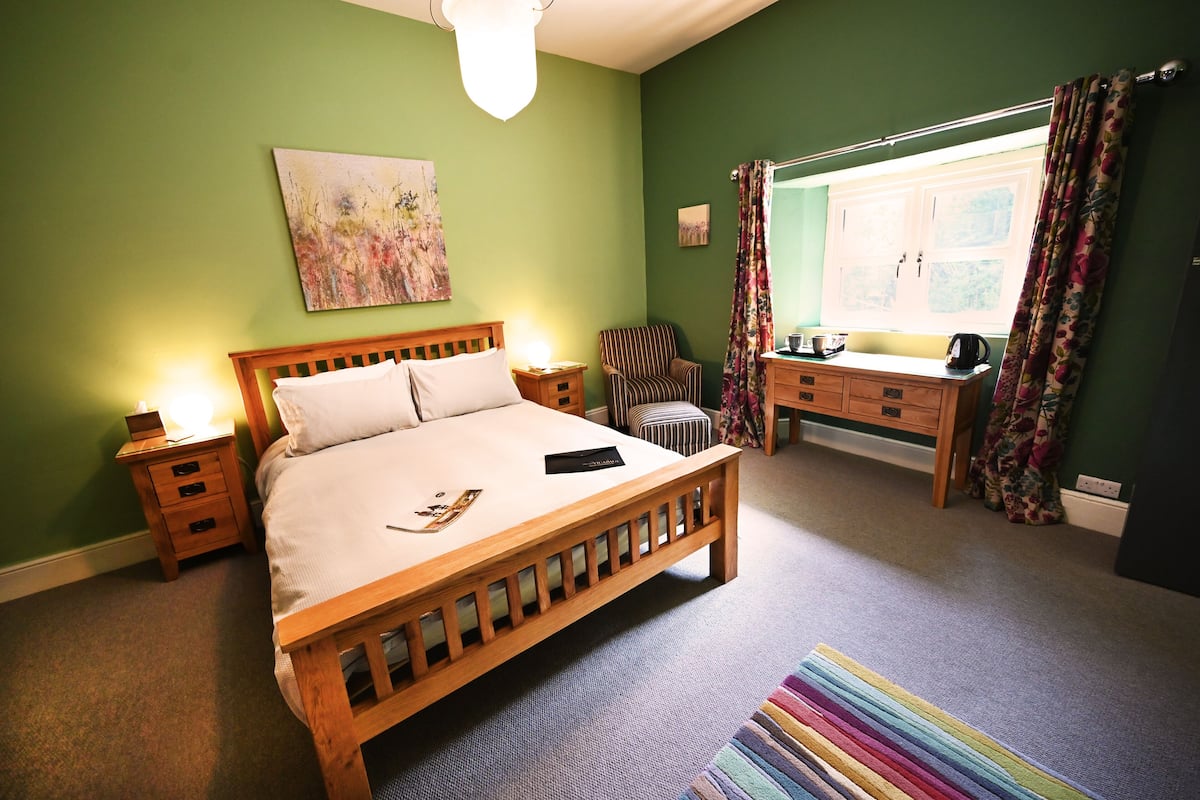 A bedroom with a wooden bed, a nightstand, a chair, a desk, and a window with curtains.