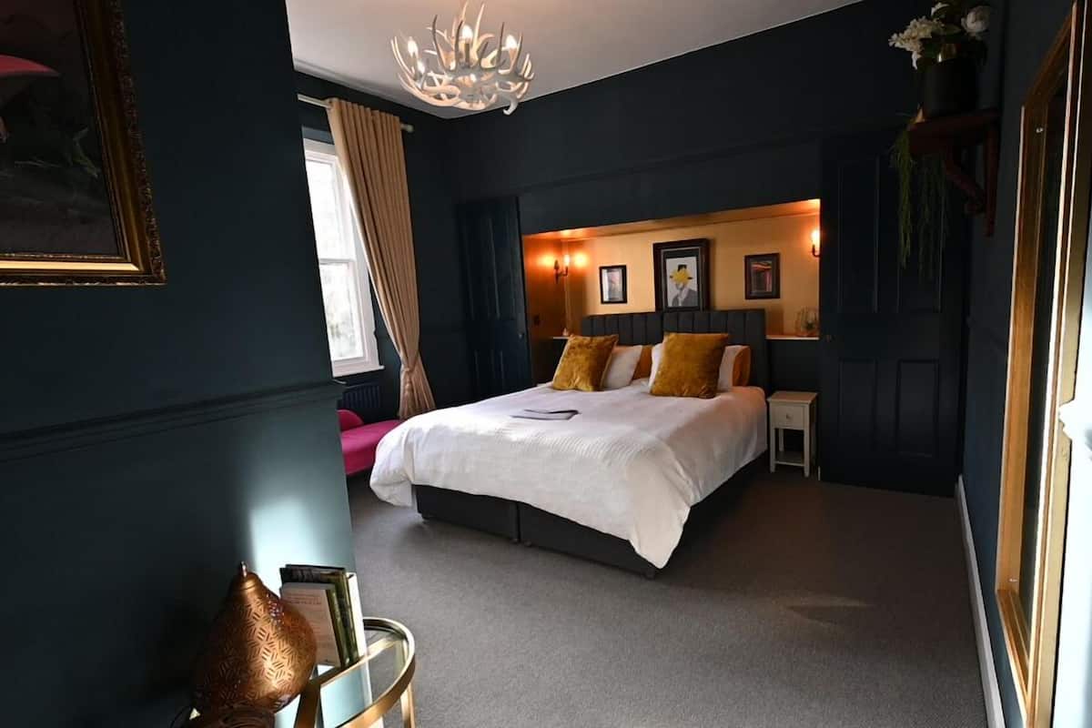 A bedroom with a large bed, a nightstand, a dresser, and a chandelier.