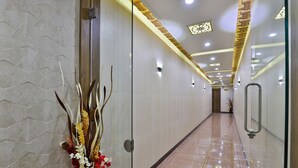 A modern hallway with a polished floor, decorative wall panels, and a glass partition with a floral arrangement. - Hotel Pearl (Vadodara)