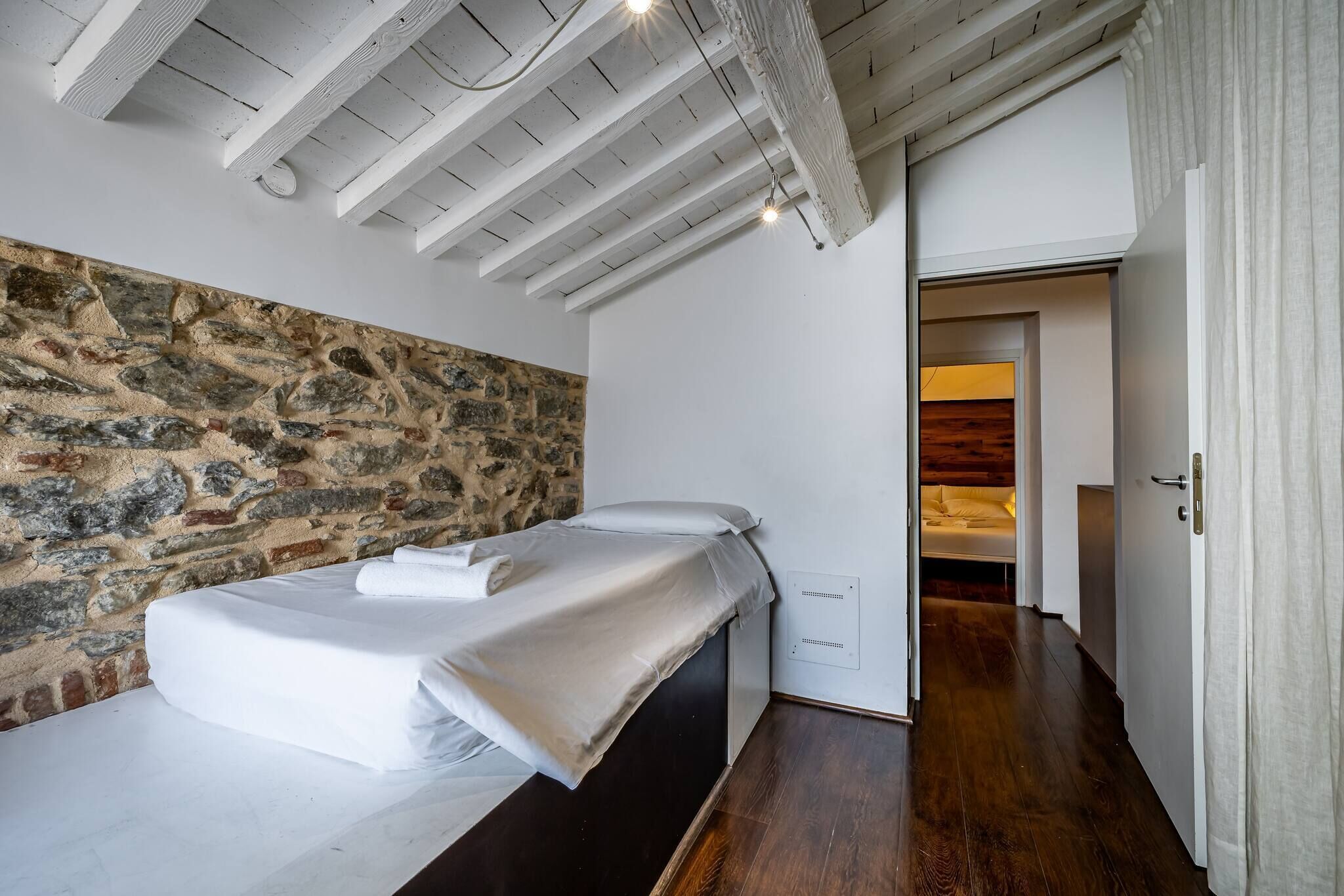 Een slaapkamer met een stenen muur, een bed met witte lakens, een houten plafond en een houten vloer.