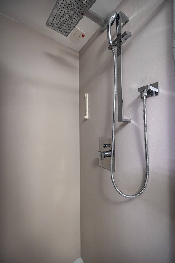 Una doccia con soffione a soffitto, un miscelatore a parete e un tubo flessibile.