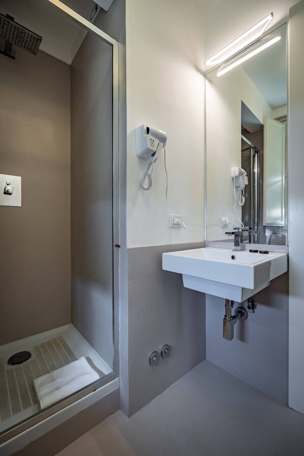 Un baño moderno con ducha, lavamanos, espejo y secador de pelo.