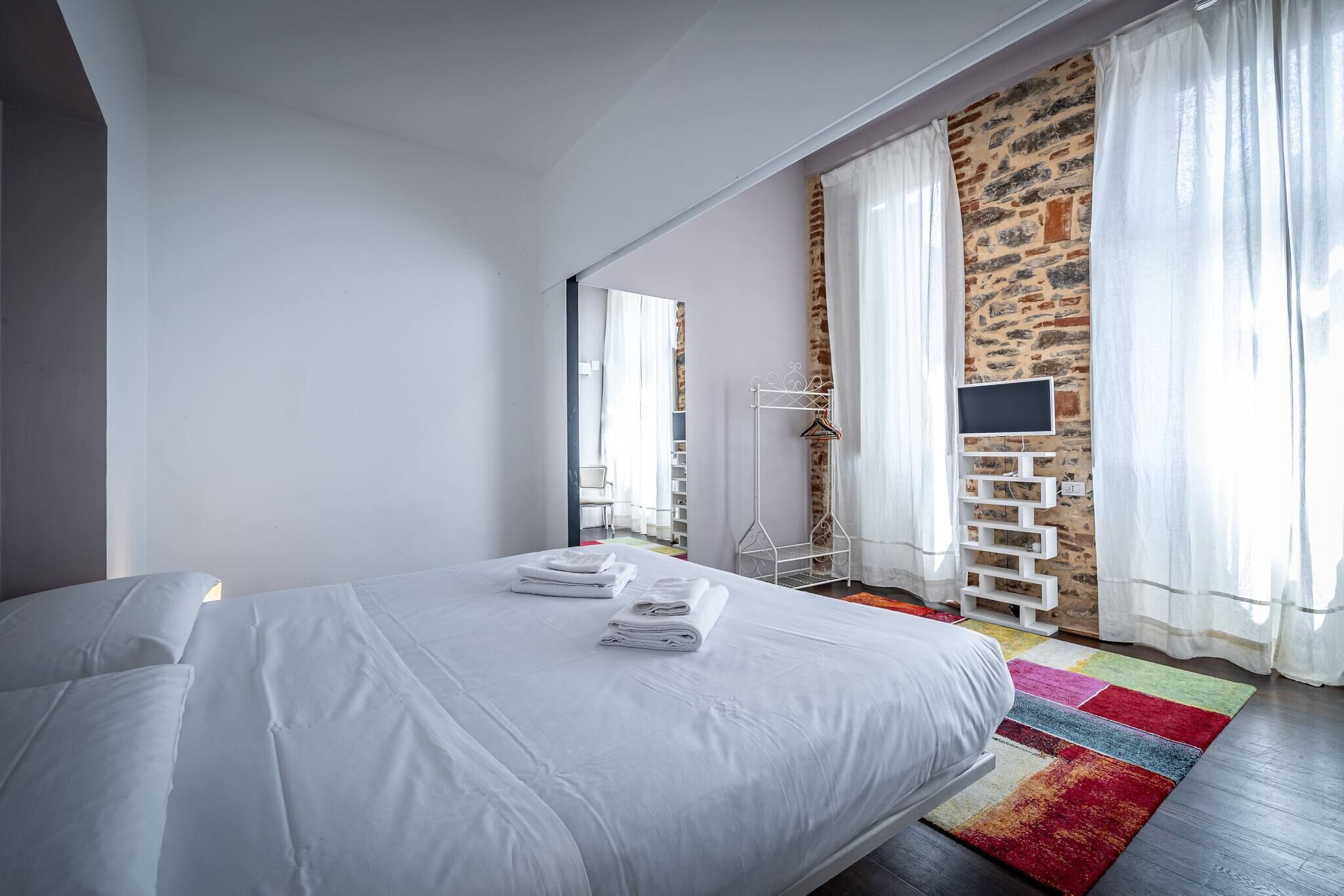 Een moderne hotelkamer met een groot bed, een flatscreen televisie, een accentmuur van steen en een kleurrijk vloerkleed.