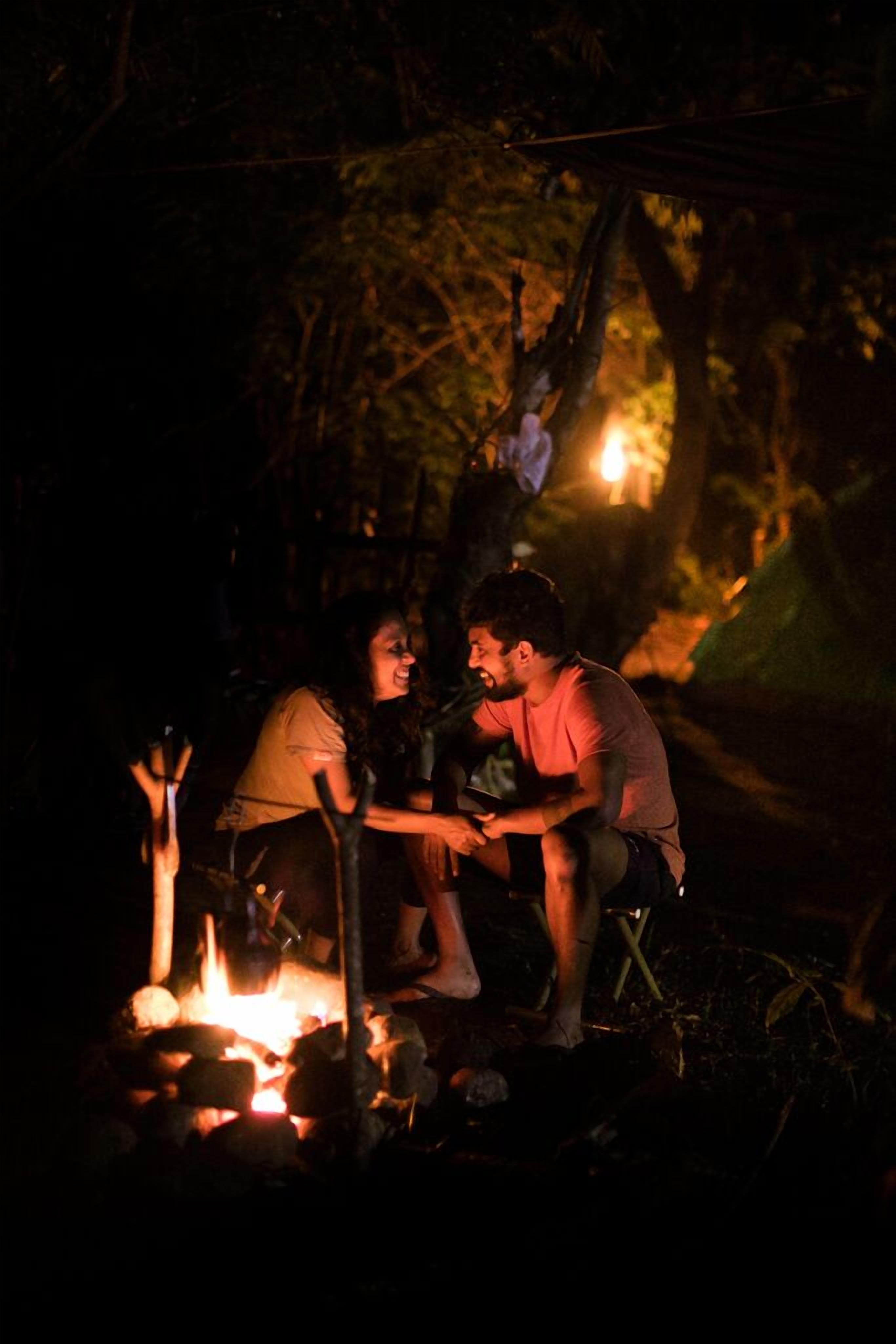 Two people sitting by a campfire in a forested area at night.