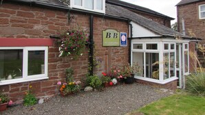 A brick building with a sign for 'Crossroads House B&B' and a small garden with potted plants and flowers. - Crossroads House (Carlisle)