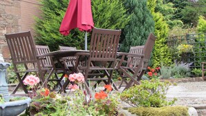 A patio with wooden chairs and a red umbrella, surrounded by potted plants and a brick wall. - Crossroads House (Carlisle)