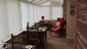 A dining area with a table set for two, a red chair, and a brick wall. - Crossroads House (Carlisle)