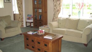 A living room with two sofas, a wooden coffee table, a glass cabinet, and a window with curtains. - Crossroads House (Carlisle)
